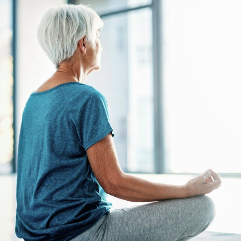 older woman sitting in front of window meditating