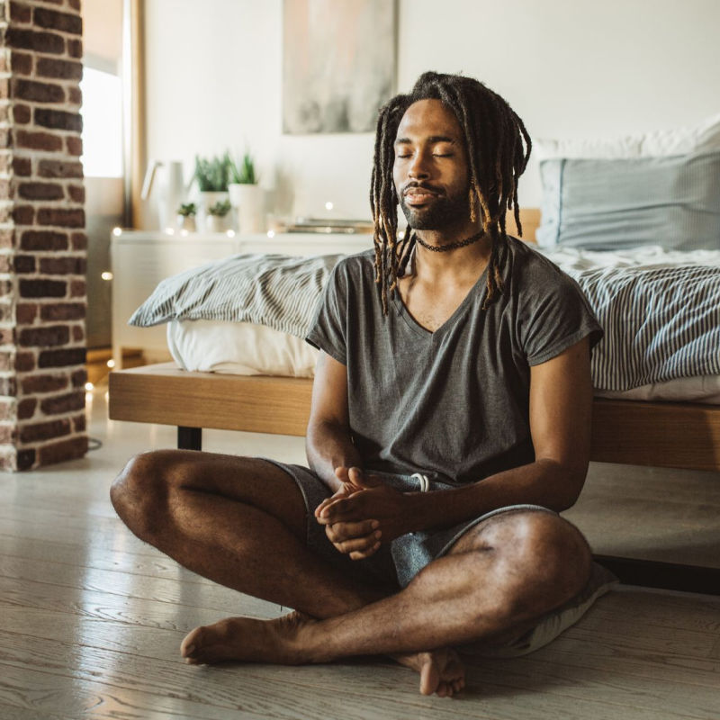 man sitting on the floor in front of his bed meditating